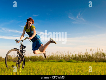 Donna felice con una vecchia bicicletta in un prato verde e salto