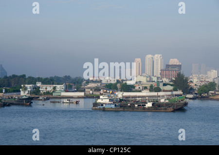 Il Vietnam, Ho chi minh city (aka saigon). Tipico saigon vista fiume con barche cargo & saigon skyline della città in distanza. Foto Stock