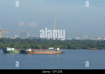 Il Vietnam, Ho chi minh city (aka saigon). Tipico saigon vista fiume con saigon skyline della città in distanza. cargo barche. Foto Stock