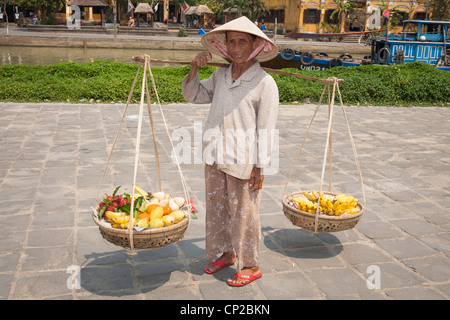 Una donna vietnamita, portando cesti di frutta, Hoi An, Quang Nam provincia, Vietnam Foto Stock