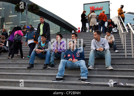 Gruppo di amici, giovani uomini asiatici, sedersi sulla procedura per il nuovo centro commerciale Westfield, Stratford, a est di Londra. Foto Stock