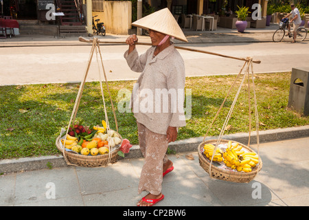 Una donna vietnamita, portando cesti di frutta, Hoi An, Quang Nam provincia, Vietnam Foto Stock