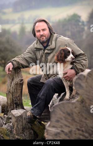 Una collina contadino con il suo cane spaniel su un albero caduto in Wales UK Foto Stock