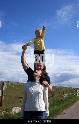 3 anno vecchia ragazza in piedi sul suo padri spalle mentre sua madre guarda in alto Foto Stock