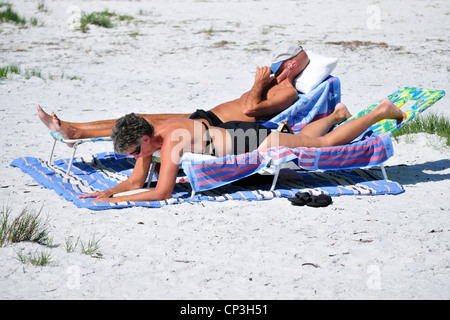 Paio di rilassarsi sulla spiaggia. Lettura di donna, uomo del posticipo Foto Stock