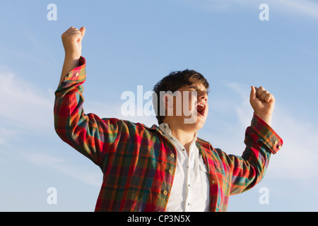 Un grido di gioia - il giovane ragazzo adolescente con bracci sollevati feeling free. Sunny esterna di estate sparato contro un cielo blu. Foto Stock