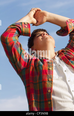 Giovane uomo di yoga - ragazzo adolescente con bracci sollevati facendo esercizi di meditazione. Divertente estate outdoor sparato contro un cielo blu. Foto Stock