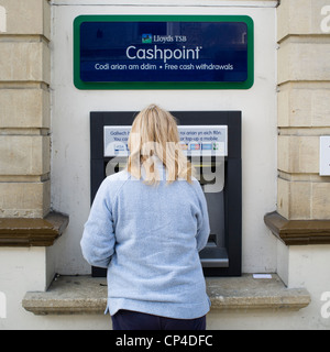 Una vista posteriore di una donna con un foro nella parete ATM Lloyds TSB Bank bancomat, REGNO UNITO Foto Stock