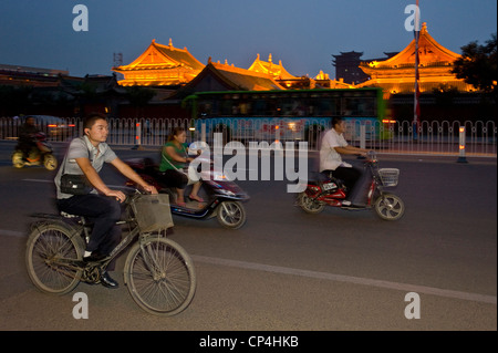 Moto e Biciclette che viaggiano lungo una delle strade principali di Hohhot con motion blur e il flash fill al crepuscolo. Foto Stock