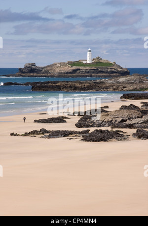 Una solitaria figura waliking accanto a rocce sulla spiaggia Gwithian, Cornwall, con faro Godrevy in background Foto Stock