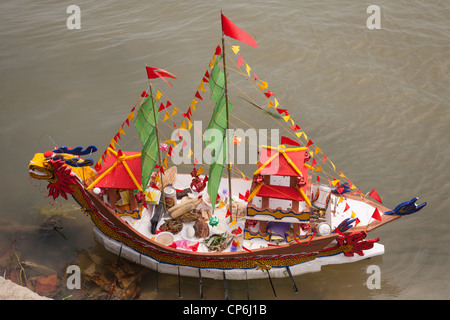 Una replica in miniatura barca modello, caricato con i religiosi offerte per la dea del mare, su Thu Bon River, Hoi An, Vietnam Foto Stock