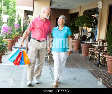Senior donna su una shopping spree guarda al suo bel marito che trasportano le valigie. Foto Stock