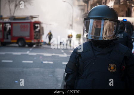 Un funzionario di polizia blocca la strada mentre i vigili del fuoco di mettere fuori un incendio impostare dai manifestanti durante uno sciopero generale in Barcellona, Spagna. Foto Stock