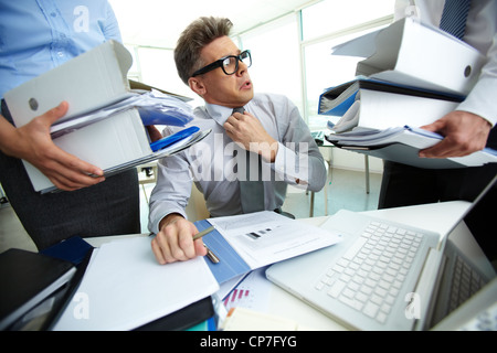 Scioccato ragioniere guardando enormi cumuli di documenti detenuti dal suo partner Foto Stock