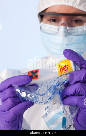 Foto di un laboratorio forense tecnico di indumenti da lavoro protettiva esaminando un contenitore in plastica che è bianco in polvere Foto Stock