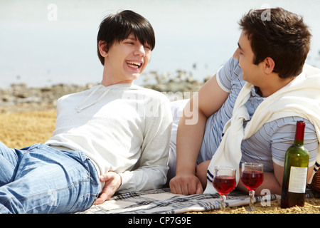 Ridendo coppia gay avente un buon tempo a bere vino rosso a beach Foto Stock