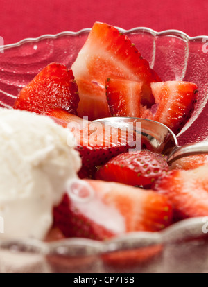 Piatto di vetro con fresco fragole a fette frutti contro una tovaglia rossa con gelato Foto Stock