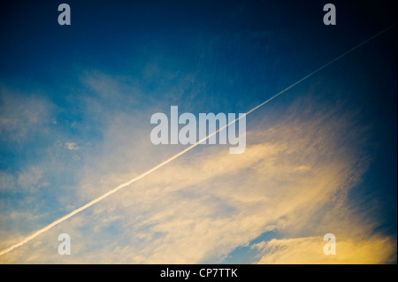 Linea aerea commerciale jet contrails attraverso un chiaro Tramonto Tramonto cielo blu Foto Stock