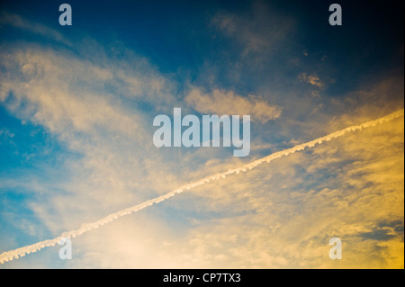 Linea aerea commerciale jet contrails attraverso un chiaro Tramonto Tramonto cielo blu Foto Stock