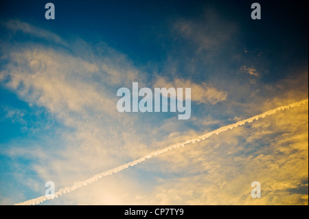 Linea aerea commerciale jet contrails attraverso un chiaro Tramonto Tramonto cielo blu Foto Stock