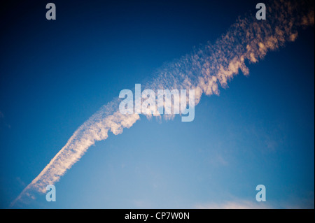 Linea aerea commerciale jet contrails attraverso un chiaro Tramonto Tramonto cielo blu Foto Stock