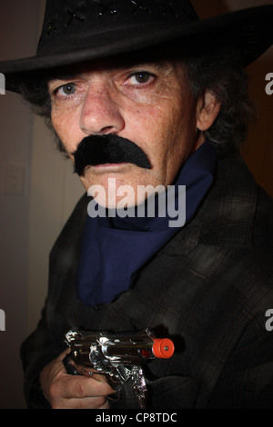 A cinquanta anni di vecchio uomo vestito da cowboy per una festa in costume verticale di sfondo semplice BDA Foto Stock