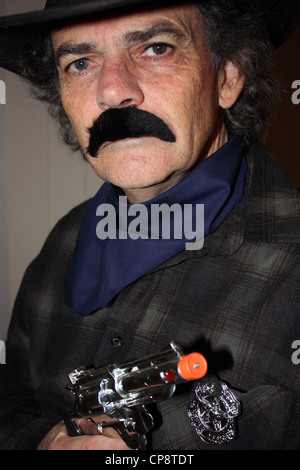 A cinquanta anni di vecchio uomo vestito da cowboy per una festa in costume verticale di sfondo semplice BDA Foto Stock