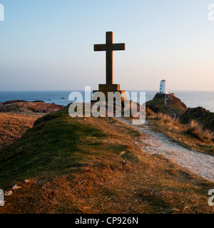 Vista guardando il mare da Llandwyn isola con una croce in primo piano e un faro in lontananza. Foto Stock