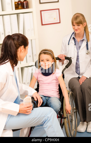 Piccola ragazza ferita su una sedia a rotelle con i medici presso ufficio medico Foto Stock