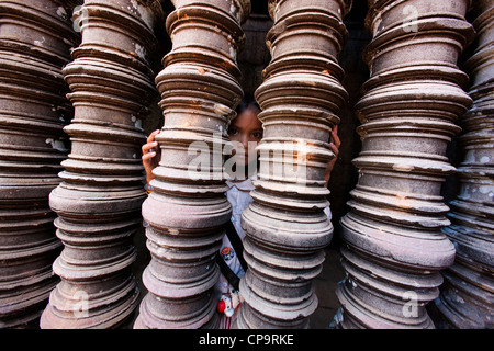 Ragazza asiatica guardando fuori da dietro una fila di arenaria, balaustre di colonne in una finestra del tempio di Angkor Wat, Siem Reap, Cambogia Foto Stock