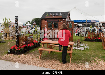 Donna che lavorano in caso di vendita, in piedi dal commercio stand promozione mobili da giardino & ornamenti decorativi - RHS Tatton Park Flower Show, Inghilterra, Regno Unito. Foto Stock