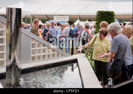 La folla di persone la visualizzazione di brillare giardino per il Cancer Research UK, come donna getta moneta nello stagno di acqua - RHS Flower Show, Tatton Park, Cheshire, Inghilterra. Foto Stock