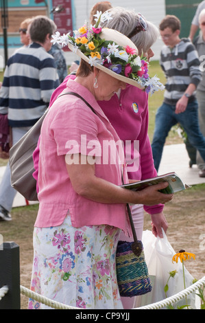 Close-up di lady indossando cappello di paglia decorato con colorati fiori estivi, in piedi e la lettura di libro guida - RHS Flower Show Tatton Park, Cheshire, Regno Unito Foto Stock
