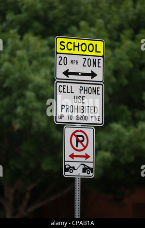 Il segno inviato dalla scuola elementare con la scuola zona limite di velocità, mostrando che il parcheggio non è consentito e ammende per l uso del telefono cellulare Foto Stock