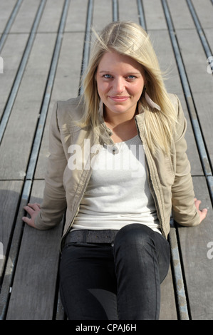 Giovane e bella donna bionda seduto su un pavimento di legno fuori nel sole Foto Stock