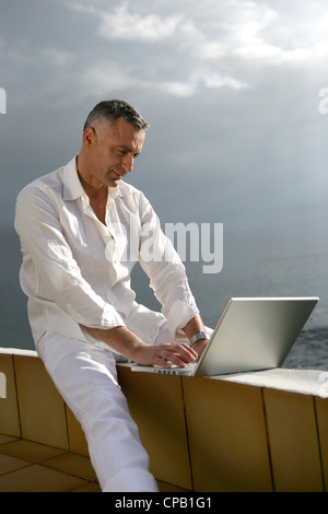 Uomo al lavoro sul suo computer portatile dall'oceano Foto Stock
