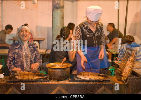Preparazione alla griglia e di pesce speziati snack alimentare alla ben nota Strada Zhengning notte food street market a Lanzhou. Foto Stock