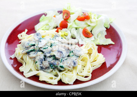 Tagliatelle e rabboccato con un semplice funghi, cipolla, prezzemolo e salsa alla panna, servito con un'insalata leggera. Foto Stock