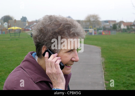 Una vecchia donna sorridente e a parlare su un telefono mobile Foto Stock