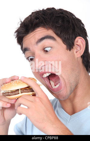 Giovane uomo prendendo un esagerato boccone fuori di un hamburger Foto Stock