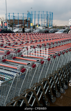 Carrelli vuoti schierate al di fuori del supermercato con gasometro in background Foto Stock