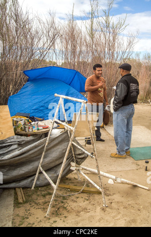 Un americano africano di beneficenza rappresentante la Chiesa parla con un uomo senza tetto che vivono in un accampamento all'aperto in un deserto città Foto Stock