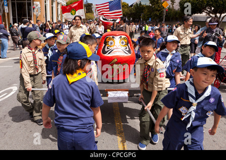 Japanese-American boy scout portando una grande bambola Daruma figura durante un festival culturale parade Foto Stock