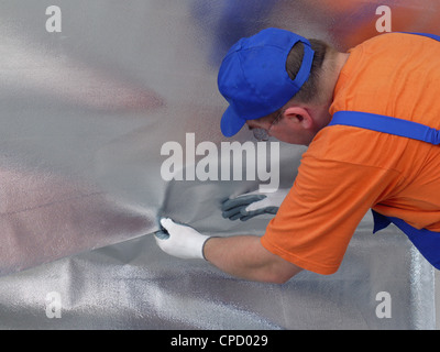 Operaio edile apposizione di vapore lamina di isolamento sotto isolato termicamente la superficie attico Foto Stock