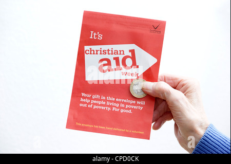 Donna che mantiene la donazione di un £2 moneta per una raccolta di beneficenza busta per Christian Aid settimana Foto Stock