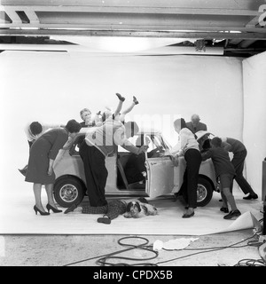 1960s. Gruppo di attori in un studio fotografico fingere che stanno cercando qualcosa in un mini auto. Foto Stock