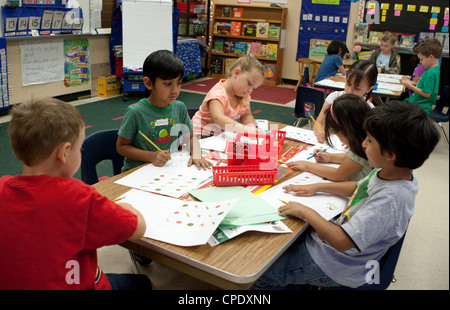 Multi-gruppo etnico di asilo gli studenti lavorano in un grande tavolo in Texas pubblico scuola elementare classroom Foto Stock