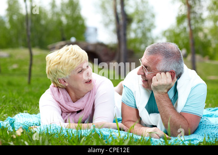 Felice Coppia matura giacente su erba e parlando in campagna Foto Stock