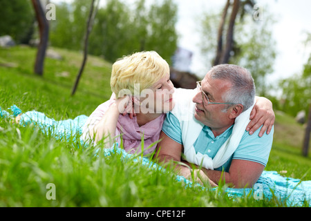 Felice Coppia matura giacente su erba e guardando ogni altra in campagna Foto Stock