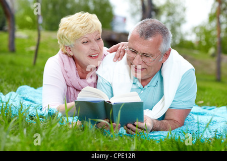 Felice Coppia matura giacente su erba e la lettura di un libro in campagna Foto Stock